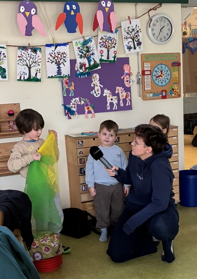 Eine Reporterin von Radio Bremen befragt 2 Kinder aus der Kita-Gruppe, wobei der eine Junge zwei Jongliertücher in der Hand hält und der andere aufgeregt zu der Reporterin schaut.