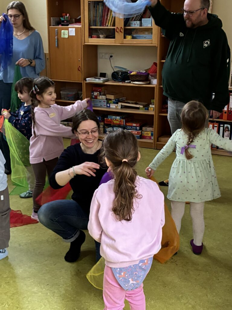 Die Zirkuspädagogin erklärt den Kita-Kindern mit einem Lächeln auf dem Gesicht eine Jonglierübung mit Tüchern.