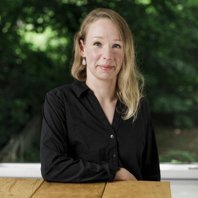 Nadine Wernickpe, pädagogische Gesamtleitung der Hans-Wendt gGmbH, mit freundlichem Gesicht an einem Tisch lehnend